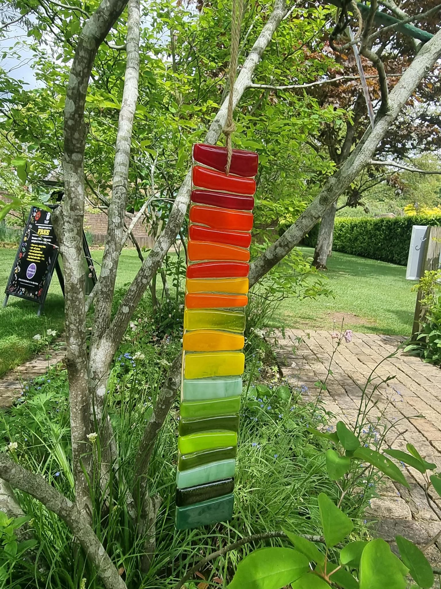 Colorful glass sculpture hanging among trees in a garden